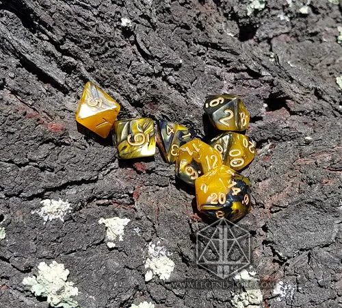Set di sette dadi poliedrici Ashes of War, oro e nero marmorizzati con numeri dorati, su corteccia con licheni