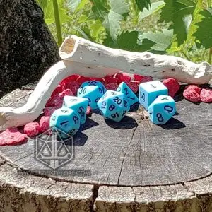 Set Broken Sky di sette dadi poliedrici azzurri opachi con numeri blu scuro su un ceppo, con legno secco e sassi rossi
