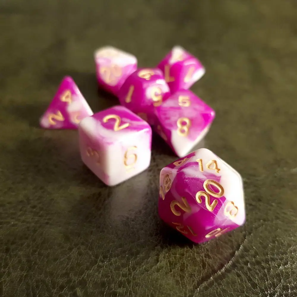 Candy RPG dice set: seven pink and white swirled polyhedral dice with gold numbers on a dark green leather surface