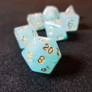 Set di dadi GdR Celestia: dadi poliedrici azzurro ghiaccio smerigliati con numeri dorati, D20 in primo piano su feltro scuro