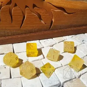 Set di dadi GDR Cloudy Topaz: sette dadi poliedrici giallo traslucido velato con numeri dorati su piastrelle di pietra