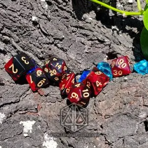 Set di dadi GdR Hell: sette dadi poliedrici bicolore rossi e neri con numeri dorati su corteccia, accanto a gemme blu