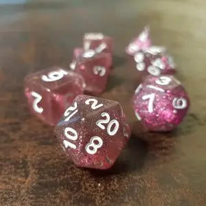 Set di dadi GdR Hippocras: dadi poliedrici rosa trasparenti con glitter e numeri bianchi su un tavolo di legno