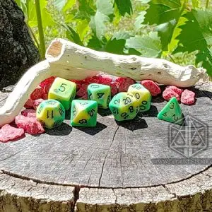 Set di dadi GDR Infested Pond: sette dadi poliedrici bicolore verde e giallo su un ceppo con legno e sassi rossi