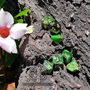 Set di dadi GDR Jungle: sette dadi poliedrici marmorizzati verde e nero con numeri dorati su corteccia accanto a un fiore rosa