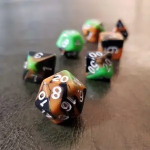 Set di dadi GdR Lawn and Asphalt: sette dadi poliedrici opachi a strisce arancio, nere e verdi con numeri bianchi su pelle scura