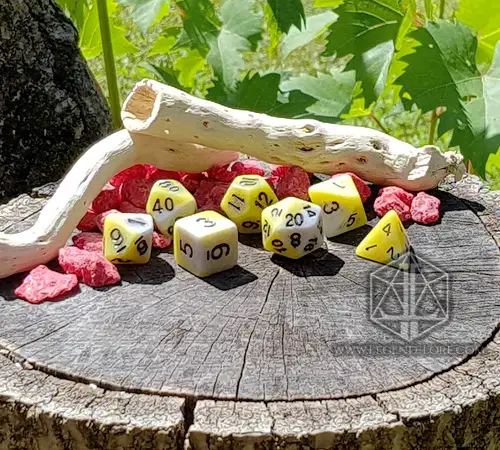 Pale Death set of seven polyhedral dice in white and yellow with black numbers on a tree stump with driftwood and red stones