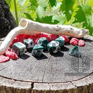 Set di sette dadi poliedrici Persistent Acid bicolore verde e bianco su un ceppo con legno chiaro e sassi rossi