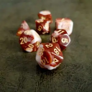 Set di dadi GdR Raspberry: sette dadi poliedrici rosso scuro e bianco marmorizzati, numeri dorati, su pelle verde