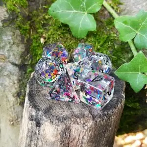 Set di sette dadi poliedrici Shooting Stars trasparenti con scaglie glitter arcobaleno e numeri neri su un ceppo muschioso