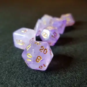 Set di dadi GdR Winter Flowers in resina lilla e viola effetto ghiaccio con numeri dorati, D20 in primo piano su feltro verde scuro