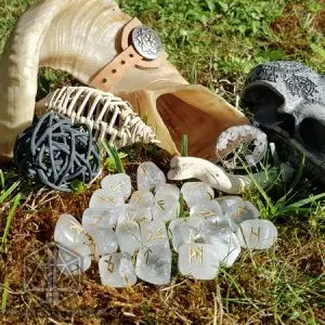Rune divinatorie Energy Spikes in quarzo trasparente con simboli dorati sull'erba, accanto a un corno e un teschio intagliato