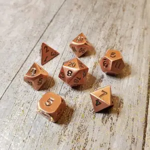 Set di sette dadi poliedrici in metallo ramato Forgotten Construct con numeri neri su legno grigio e brillantini dorati