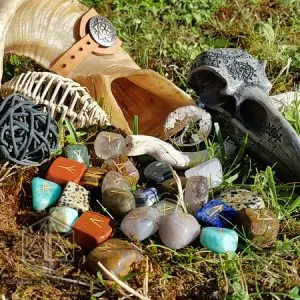 Rune divinatorie Iridescent Cornucopia: gemme miste incise con rune dorate, accanto a un corno e un teschio di corvo sull'erba