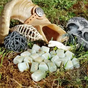 Rune divinatorie Jade Tears in pietra verde chiaro con simboli dorati sul muschio, accanto a un corno e a un teschio decorativo