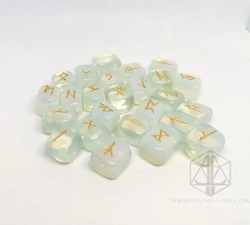 Moon Tears divination runes: translucent opalite stones engraved with gold Elder Futhark symbols on a white surface