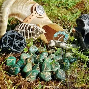 Rune divinatorie Seer Eyes in avventurina verde con simboli dorati sul muschio, tra corno, scheletro, ciondolo e teschio