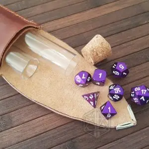 Set di sette dadi poliedrici Strange Berries in metallo viola con numeri bianchi, accanto a un astuccio in pelle e fiale