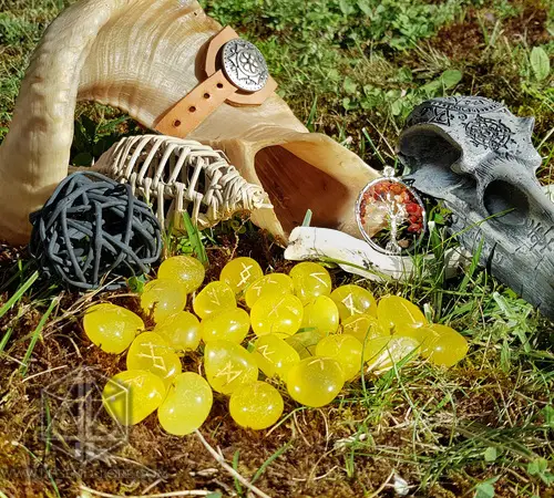Sun Tongues yellow divination rune stones with carved runes on moss, beside a horn, skull figure and tree-of-life pendant