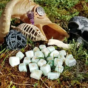 Rune divinatorie Wind Soul in amazzonite verde chiaro con simboli dorati sull'erba, accanto a corno, pendolo e teschio