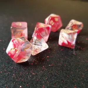Set di dadi GdR Cloudy Cherry Tree: sette dadi trasparenti con venature rosa e bianche e numeri dorati su feltro nero
