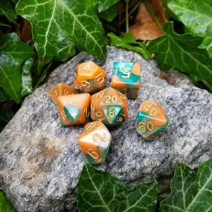 Set di sette dadi poliedrici Dusk Oasis bicolore arancio e verde con numeri dorati su una roccia tra foglie d'edera