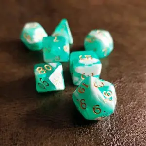 Set di dadi GDR Jelly: sette dadi poliedrici verde acqua e bianco marmorizzati con numeri dorati su pelle scura