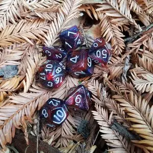 Set di sette dadi poliedrici Blood Darkness rossi e viola glitterati con numeri bianchi su aghi di sequoia secchi