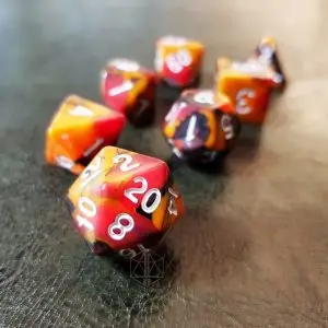 Set di dadi Cold Embers: sette dadi poliedrici opachi variegati rossi, arancioni e neri con numeri bianchi su pelle scura