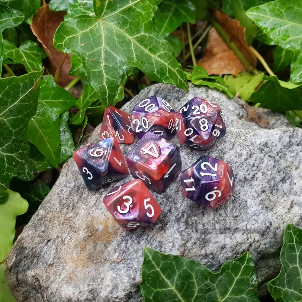 Cold Plasma RPG dice set: seven swirled red, pink and purple polyhedral dice with white numbers on a stone among ivy
