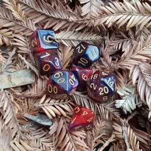 Set di dadi GDR Fire Crystal: sette dadi poliedrici rossi e neri con glitter stardust e numeri dorati su aghi di pino secchi