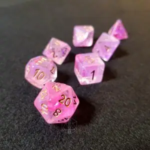 Set di sette dadi Purple Glory in resina traslucida rosa e viola effetto nebulosa con numeri dorati su feltro grigio scuro