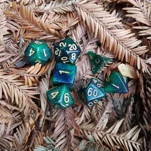 Set di sette dadi poliedrici Sprouts of Life verdi e blu glitterati con numeri dorati su aghi di sequoia secchi