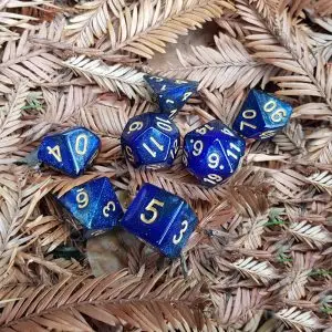 Set Starry Night di sette dadi poliedrici blu glitterati con numeri dorati su foglie secche marroni