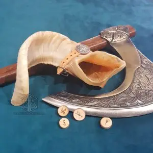 Viking Horn, corno naturale color crema con cinghia in cuoio e borchia, accanto a un'ascia incisa e rune in legno