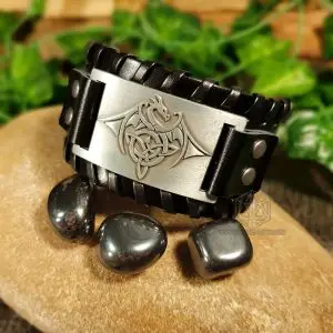 Black Draconic Protection Viking leather bracelet with silver plate showing a Celtic knot dragon, beside polished hematite stones