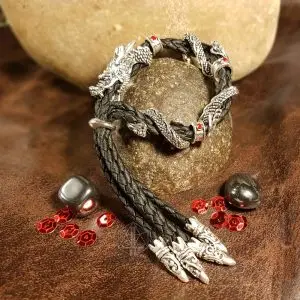 Dragon Mark bracelet of braided black leather with silver dragon beads and red gems, draped over a stone with red sequins
