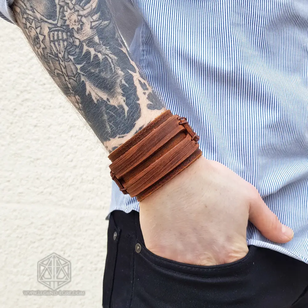 Ancient Oath Viking leather bracelet, wide brown layered cuff with laced straps, worn on a tattooed wrist