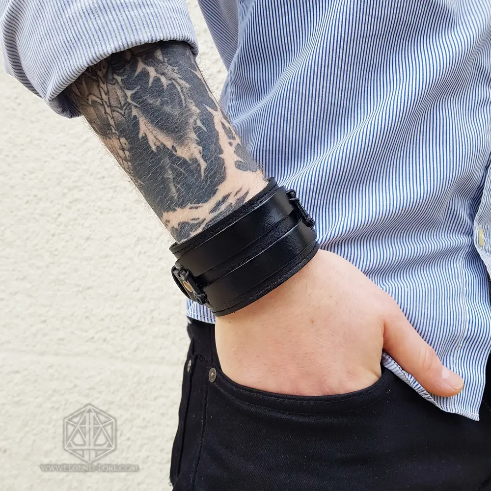 Bracciale vichingo Dark Oath, polsino largo in pelle nera con cinghie e fibbia in metallo scuro su un polso tatuato