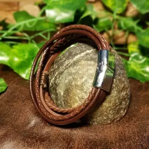 Bracciale Pathfinder Viking in pelle PU marrone con cordini intrecciati e chiusura in metallo argento, su una pietra tra l'edera
