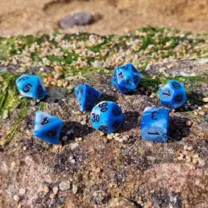 Set Blue Lagoon di sette dadi poliedrici blu e bianchi marmorizzati con numeri neri su una roccia con sabbia e muschio