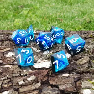 Set di dadi in resina a spigolo vivo Abyssfire Crystals, sette dadi blu e neri con numeri bianchi su corteccia