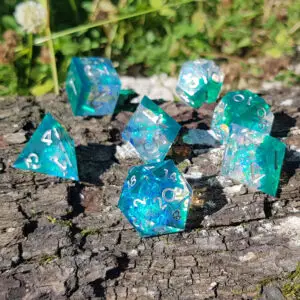 Set di dadi in resina a spigoli vivi Frostwave Crystals: sette dadi verde acqua con glitter iridescenti su corteccia
