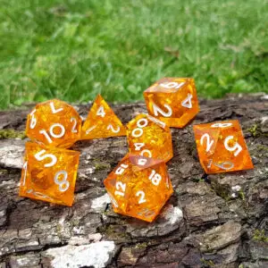 Set di dadi Emberforge Shards in resina a spigoli vivi: sette dadi arancioni con scaglie dorate e numeri bianchi su corteccia