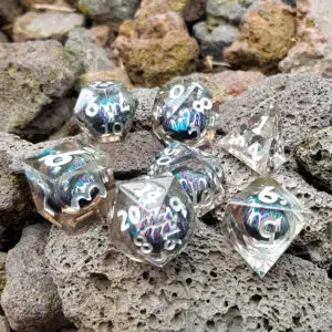 Set di sette dadi Demon Eyes in resina trasparente a spigoli vivi con occhio liquido blu e viola iridescente su roccia lavica