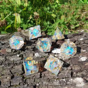 Set di sette dadi in resina a spigoli vivi Sunshard Opals, trasparenti con scaglie opaline blu e numeri dorati, su corteccia