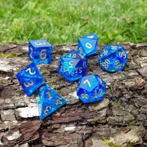 Set di sette dadi Tideborn Sapphire Shards in resina blu a spigolo vivo con numeri dorati e scaglie lucenti su corteccia