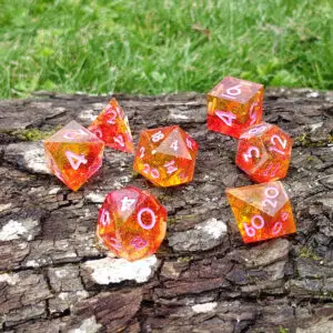 Set di sette dadi in resina a spigoli vivi Sunflare Emberstones, arancio e rossi con glitter oro e numeri rosa, su corteccia
