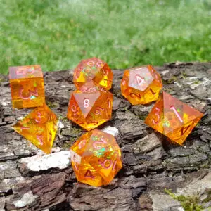 Set di sette dadi in resina a spigolo vivo Amberflare Shards, arancio trasparente con numeri rosa e glitter verdi, su corteccia