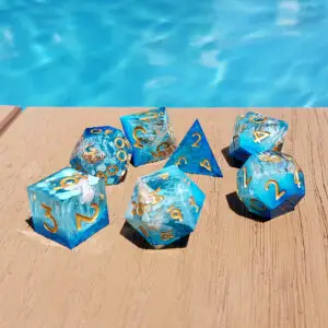 Set di sette dadi in resina a spigoli vivi Seaborn Relics, blu con conchiglie e numeri dorati, su legno accanto a una piscina